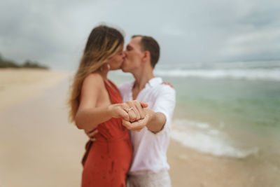 Couple standing at beach against sky