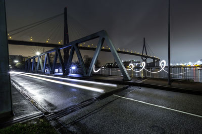 Illuminated bridge over road against sky at night