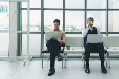 Full length of men sitting against window