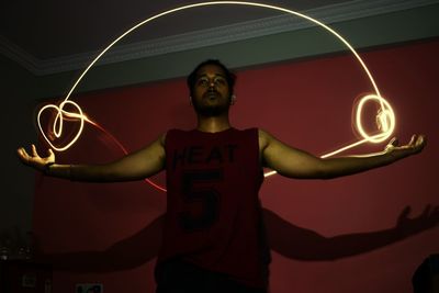 Low angle view of man standing with arms outstretched by light painting at home