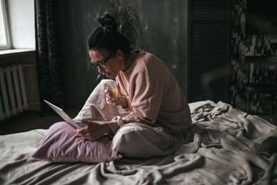 Midsection of woman reading book while sitting on bed at home