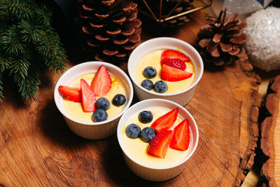 Three small servings of creme brulee with fresh blueberries and strawberries on a wooden background