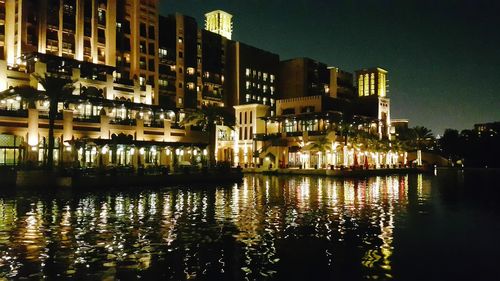 Illuminated buildings by lake in city at night