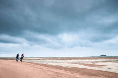 People standing at beach against cloudy sky