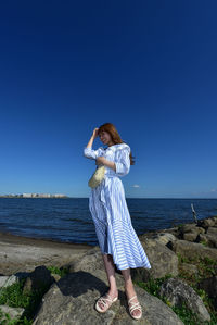 Woman standing on rock by sea against clear blue sky