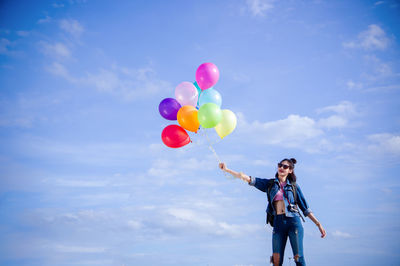 Low angle view of person holding balloons against sky