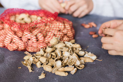 Peanut husks and a mesh bag with brown nuts on the table. baby hands peeling nuts in the background