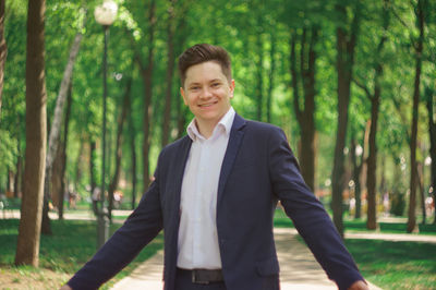 Portrait of smiling young businessman with arms outstretched standing in park