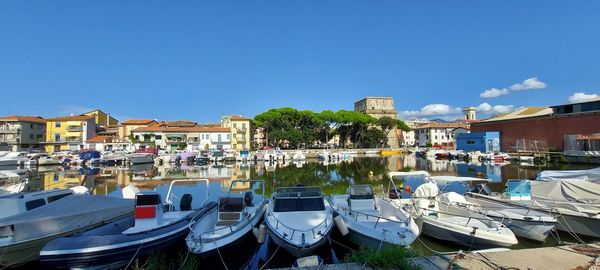 Boats moored in canal by buildings against blue sky