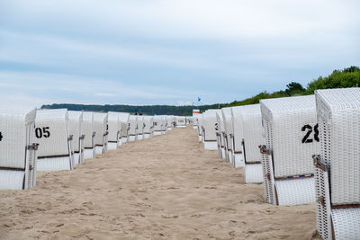 Hooded beach chairs on sand against sky