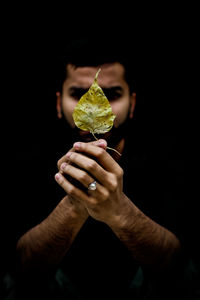 Man holding leaf in front of face against black background