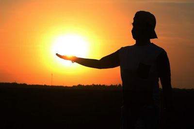 Silhouette man standing on field against orange sky