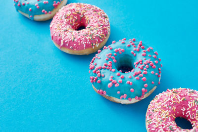 Different types of colorful donats decorated sprinkles and icing on blue background