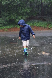 Boy wearing raincoat walking on street during rainy season