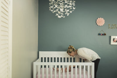 Mother looking at newborn daughter lying in crib against wall