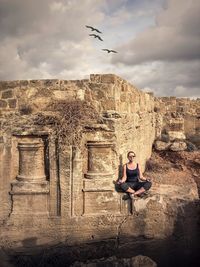 Woman sitting on stone against sky