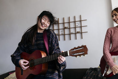 Happy friends playing guitars at home