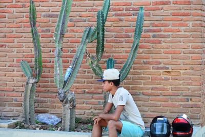 Full length of man sitting against brick wall