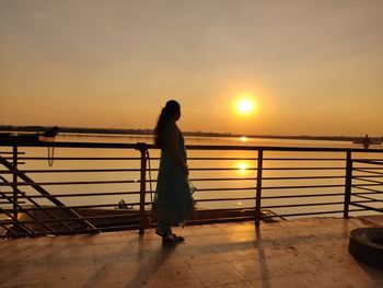 Silhouette man standing on railing against sea during sunset