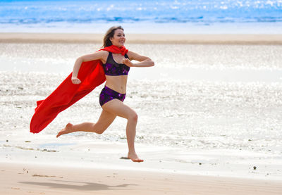 Full length of young woman wearing cape while running at beach