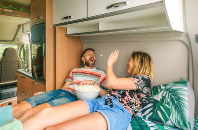 Woman throwing a popcorn into her boyfriend's mouth lying on the bed of their camper van