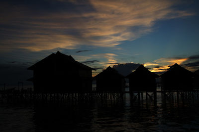 Silhouette houses by sea against sky during sunset