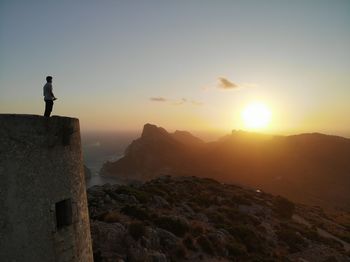 Man standing on rock against sky during sunset