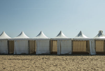 Row of umbrellas on sand at beach against clear sky