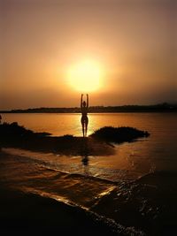 Woman doing yoga at beach against sky during sunset