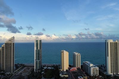 Sea by modern buildings against blue sky