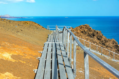 Boardwalk on cliff by sea against sky