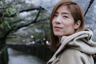 Portrait of smiling young woman against tree