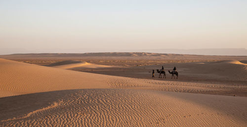 People on sand dune in desert against sky