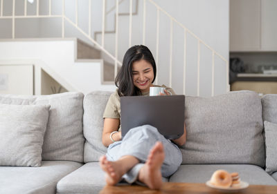 Young woman using phone while sitting on sofa at home