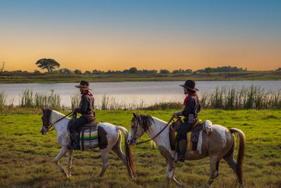 Rear view of woman riding horse on field against sky during sunset