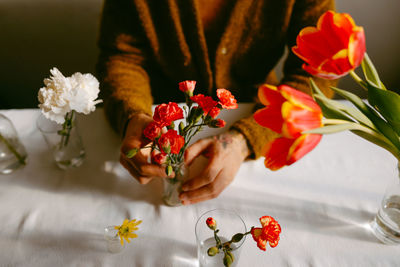 High angle of crop anonymous male florist sitting at table with carnations and tulips in glassware