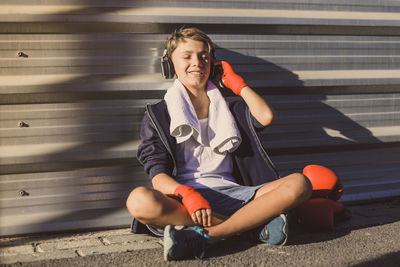 Boy sitting by wall while listening to music outdoors