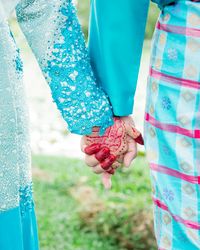 Midsection of bride and groom holding hands on field