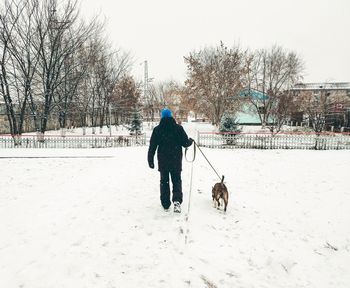 Rear view of woman with dog walking in snow