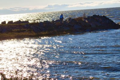 People on rocks by sea against sky