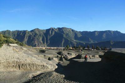 People looking at mountains against clear blue sky