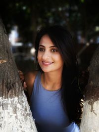 Portrait of smiling young woman against tree trunk