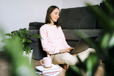 Young woman using phone while sitting on wall