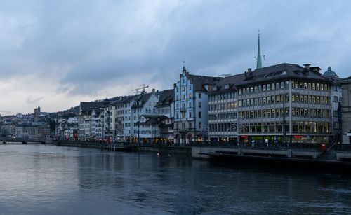 View of buildings by river against cloudy sky