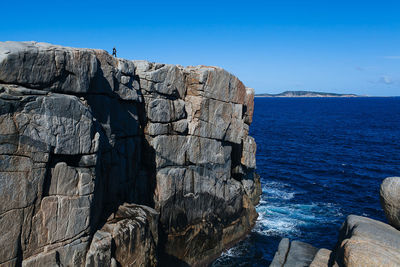 Rock formation by sea against clear blue sky