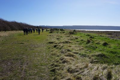 People walking on field against clear sky