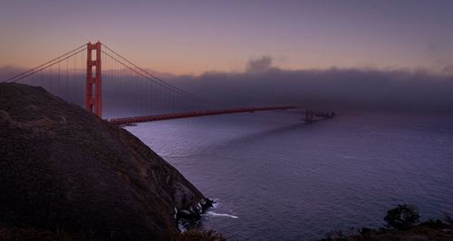 Suspension bridge over sea against sky during sunset