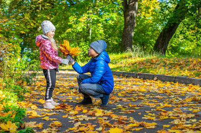 A boy squatting down gives a bouquet of yellow maple leaves a girl