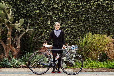 Portrait of businesswoman standing with bicycle against plants