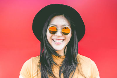 Portrait of smiling young woman wearing sunglasses against red background